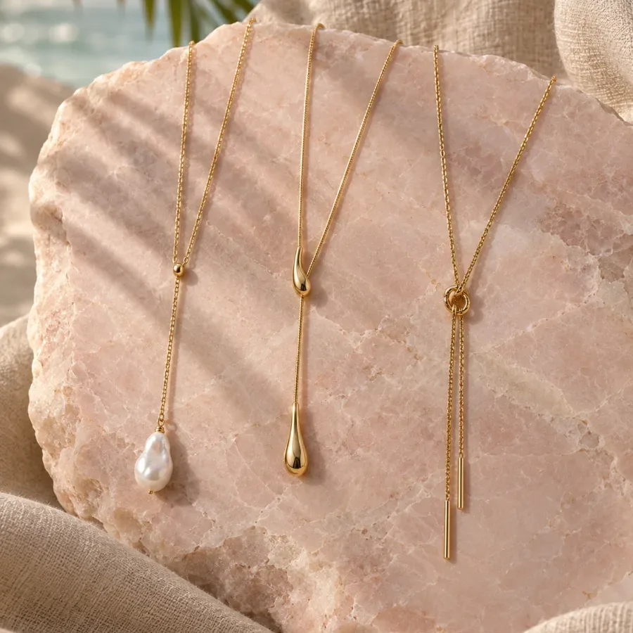 Three long gold-tone lariat necklaces arranged on pale pink stone