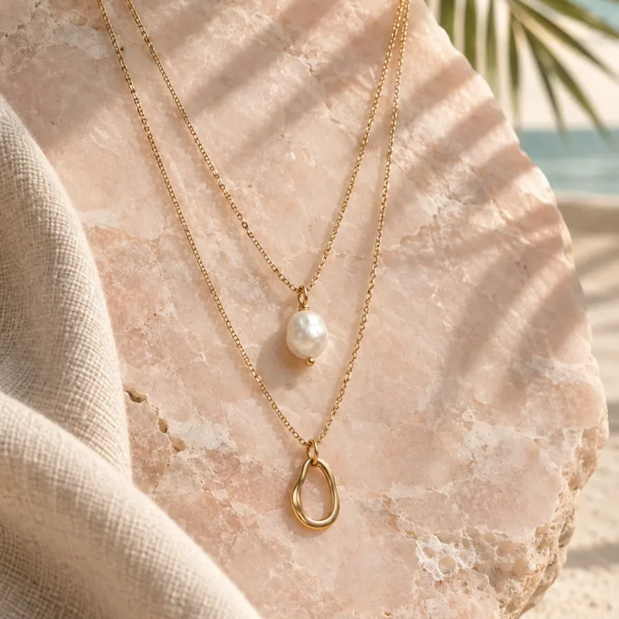 Two delicate gold-tone necklaces with pearl and sculptural pendants on pale pink stone